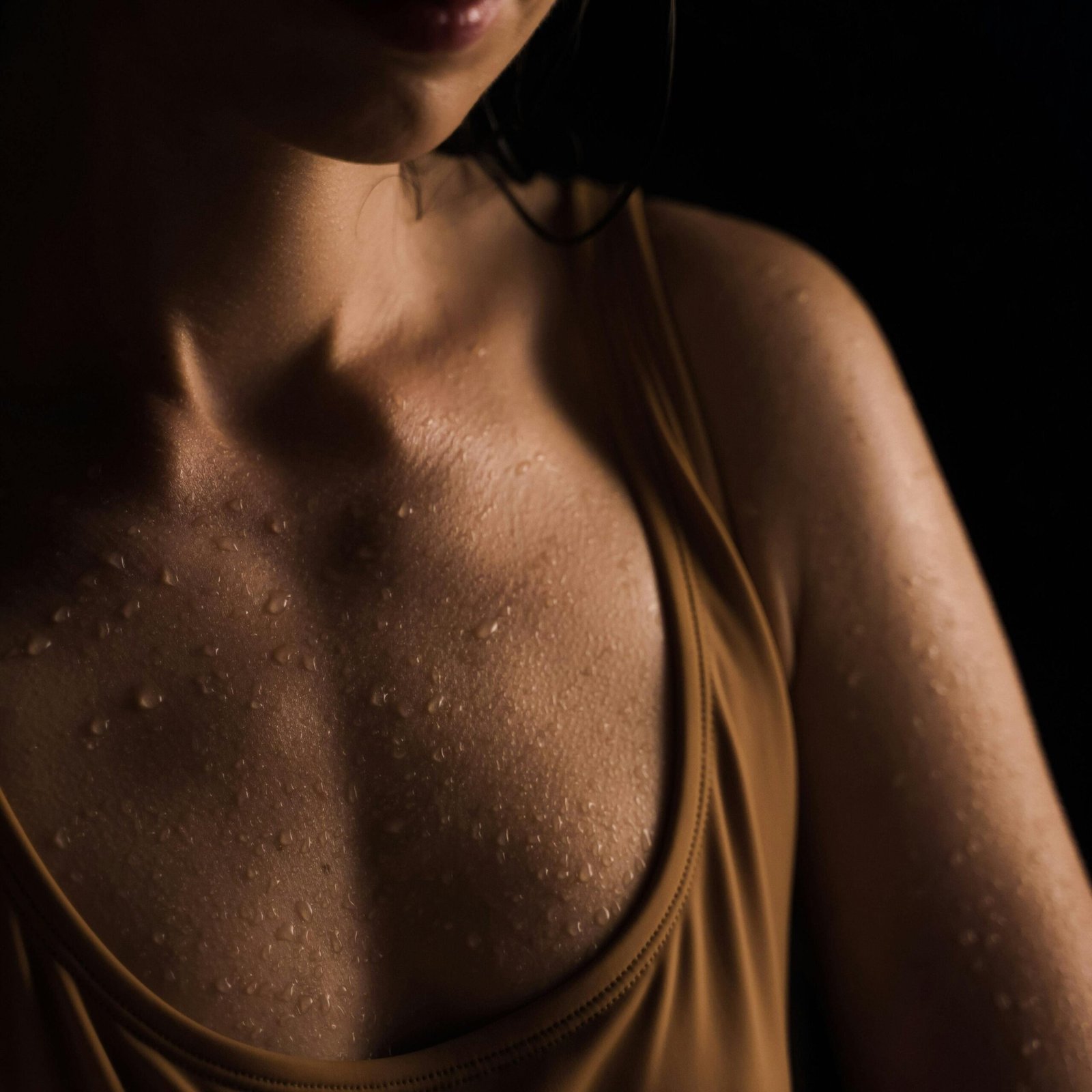 Close-up of a woman's wet skin with water droplets, set against a dark background.